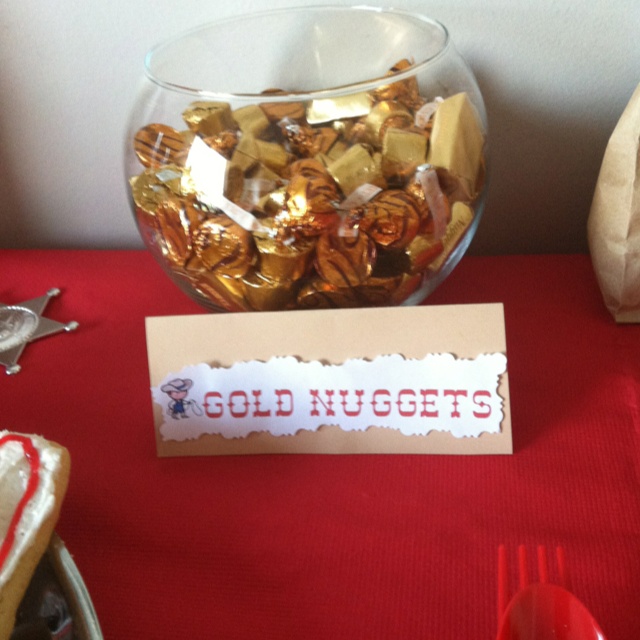 gold nuggets in a glass bowl on a red table cloth next to silverware