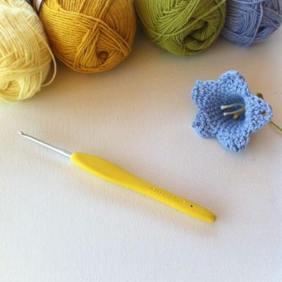 several balls of yarn next to a crochet hook with a yellow knitting needle