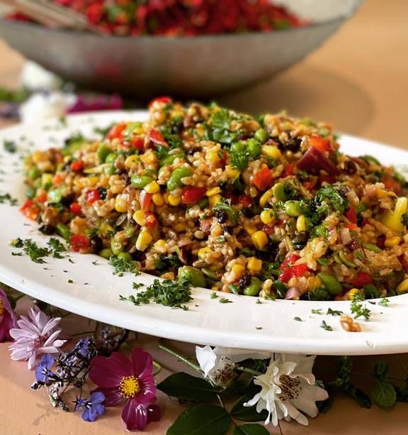 a white plate topped with salad next to a bowl filled with flowers and leaves on top of a table