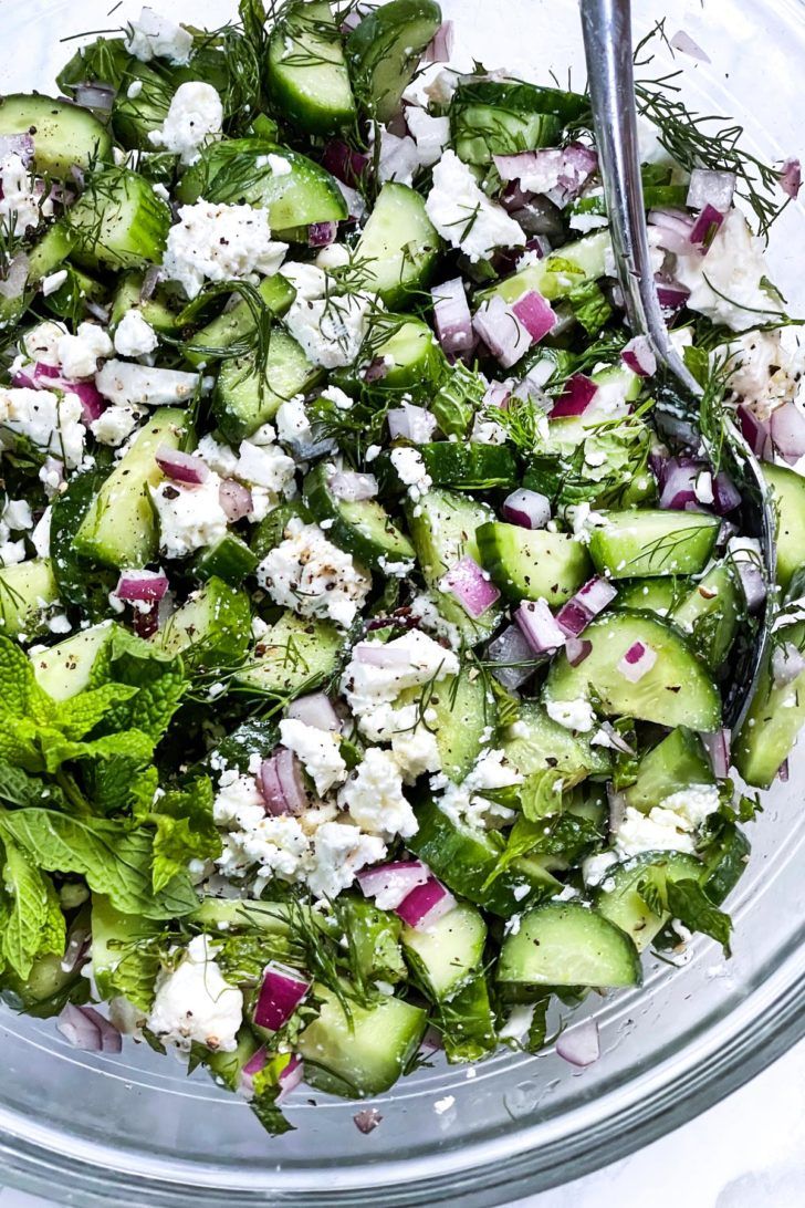 a glass bowl filled with cucumbers, feta cheese and green leafy salad