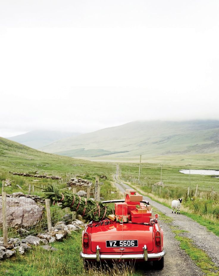 an old red car parked on the side of a dirt road next to a lush green field