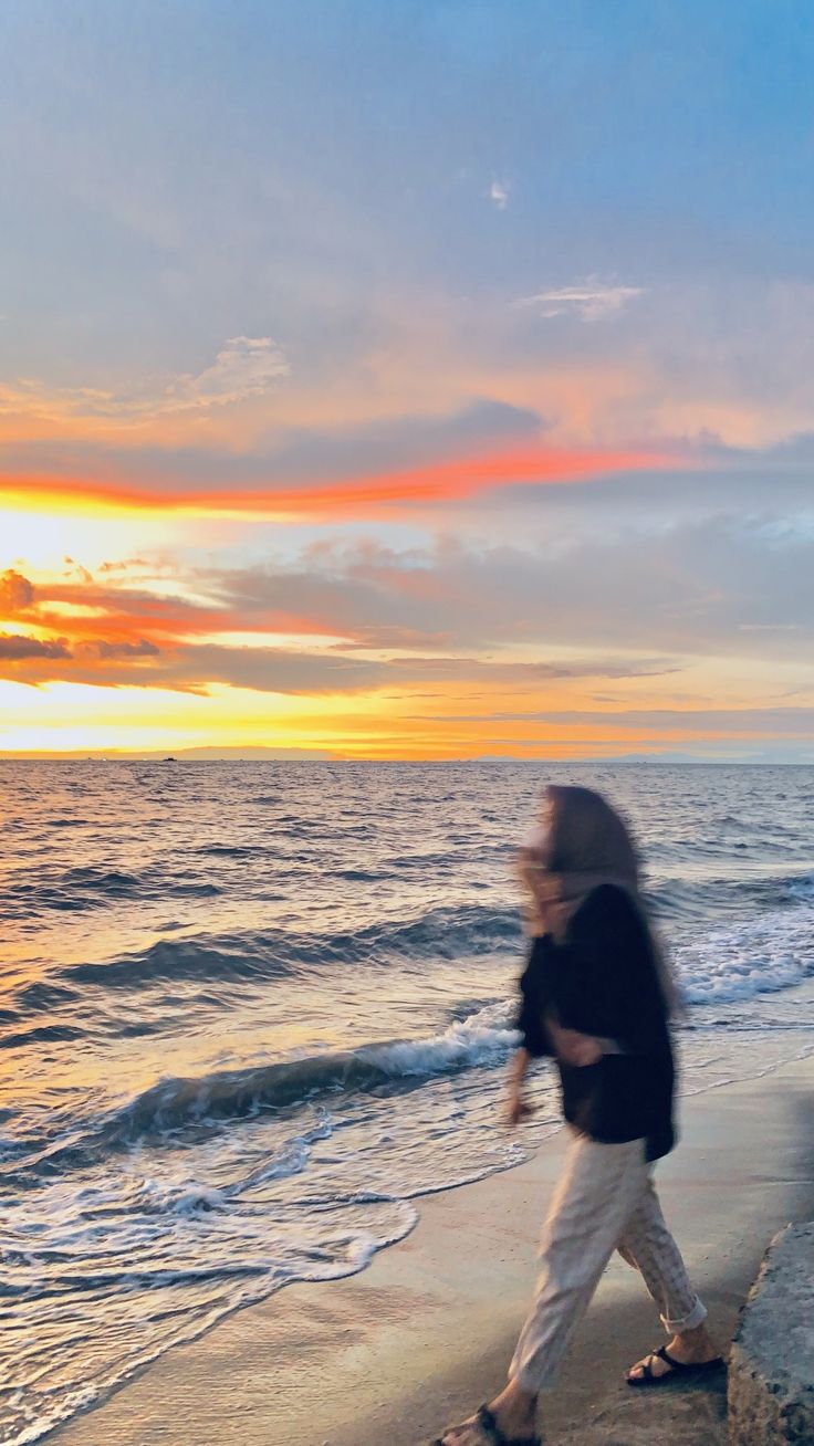 a woman walking along the beach at sunset