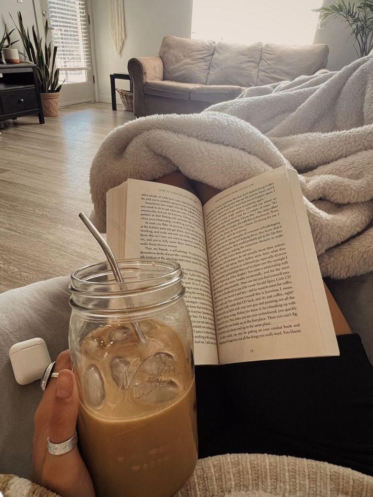 a person is holding an open book and drinking iced coffee