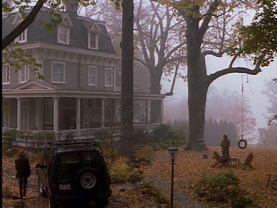 two people are standing in front of a house on a foggy day with their cars parked