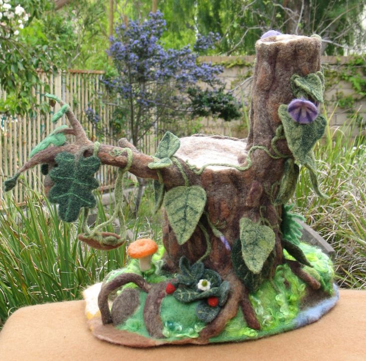 a tree house made out of felt with plants and animals on the top, sitting in a garden