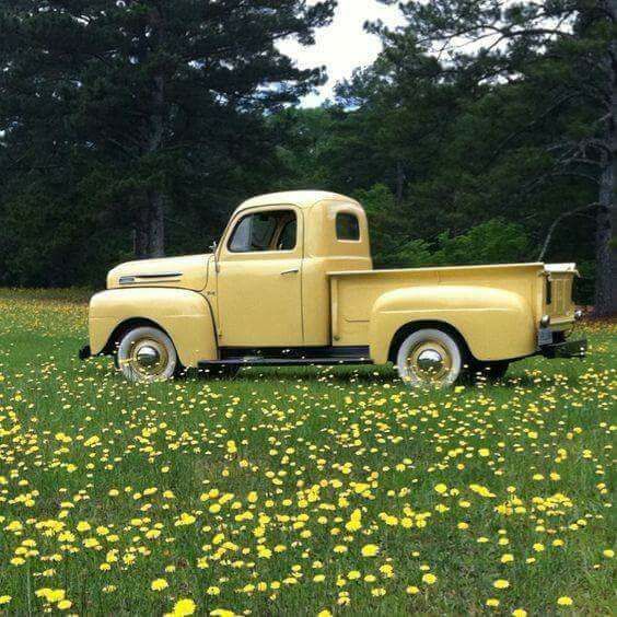 an old yellow pickup truck parked in a field full of dandelions and daisies