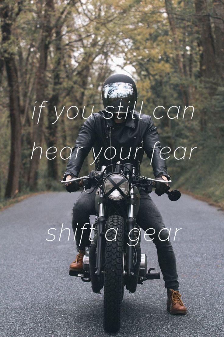 a man riding on the back of a motorcycle down a road with trees in the background