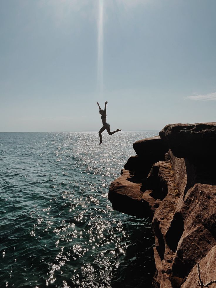 a person jumping off rocks into the ocean from a rocky cliff near the water's edge