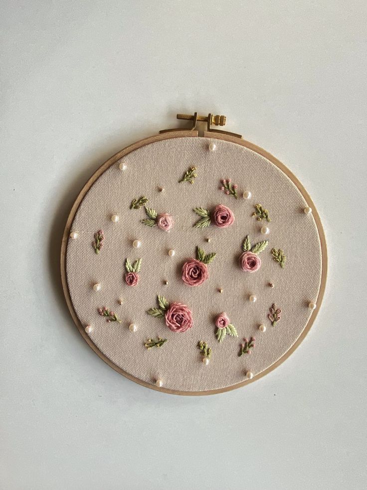 an embroidery project with pink flowers and pearls on the hoop, hanging from a white wall