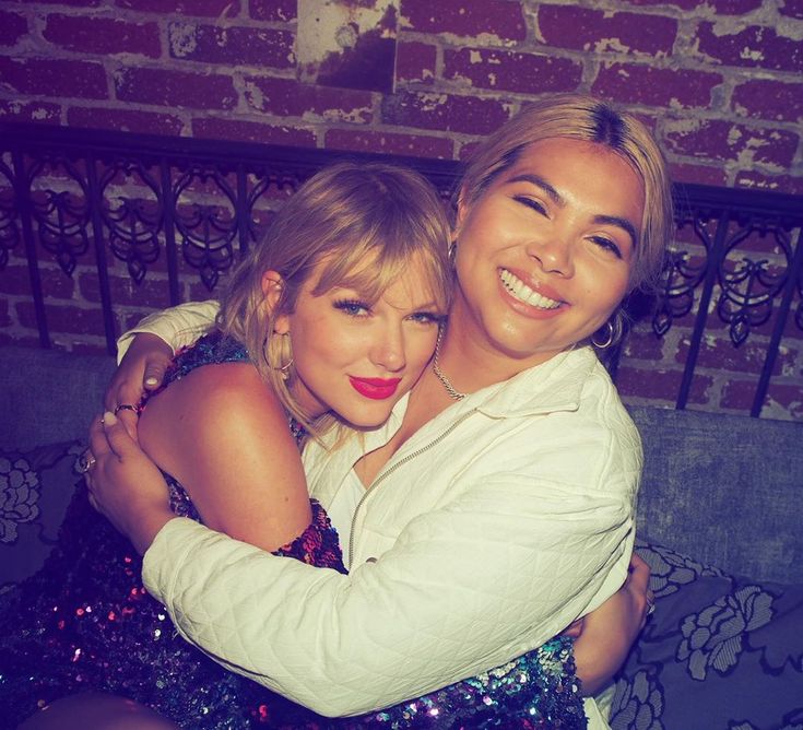 two women hugging each other in front of a brick wall