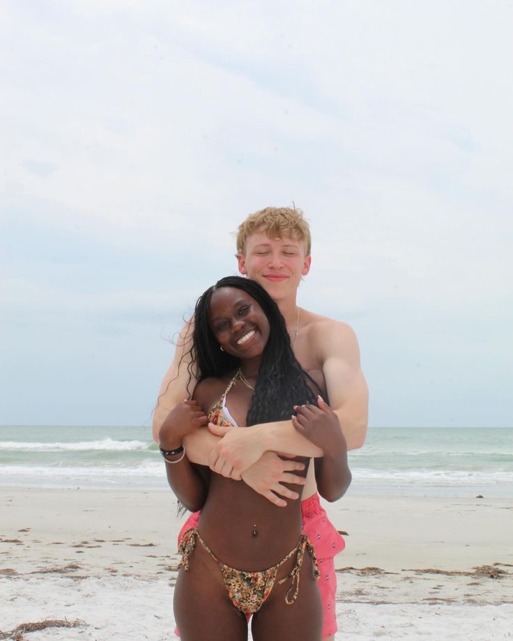 two people standing on the beach hugging each other with one person wearing a bathing suit