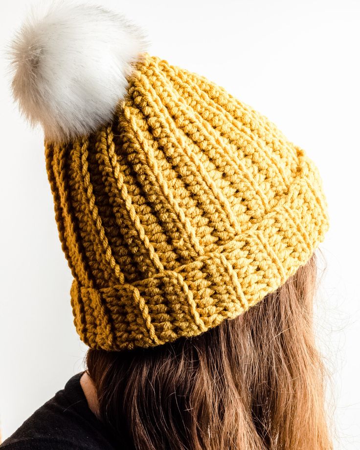 a woman wearing a yellow knitted hat with a white pom - pom