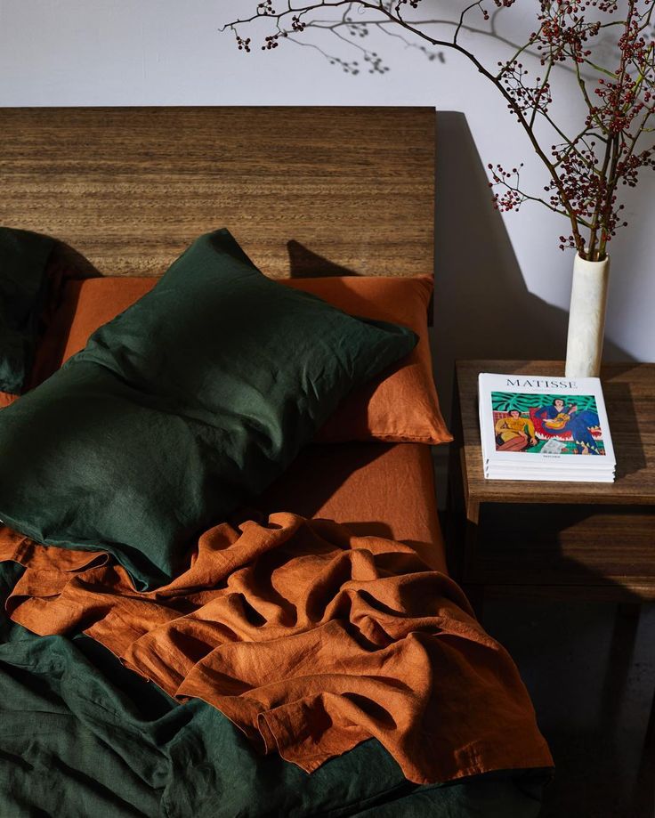 an unmade bed with green and orange sheets, pillows and a book on the end table