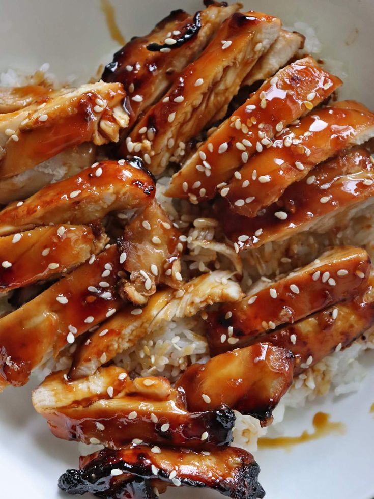 chicken with sesame seeds and sauce on top of rice in a white bowl, ready to be eaten