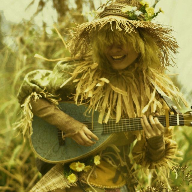 a woman wearing a straw hat and holding a guitar in her hands while walking through tall grass