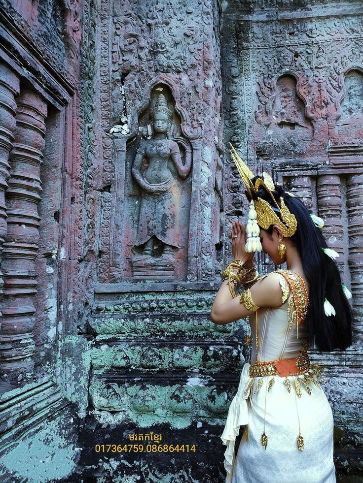 a woman dressed in traditional thai garb standing next to an old building with carvings on the walls