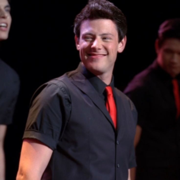 a man in a black shirt and red tie standing next to two other men on stage