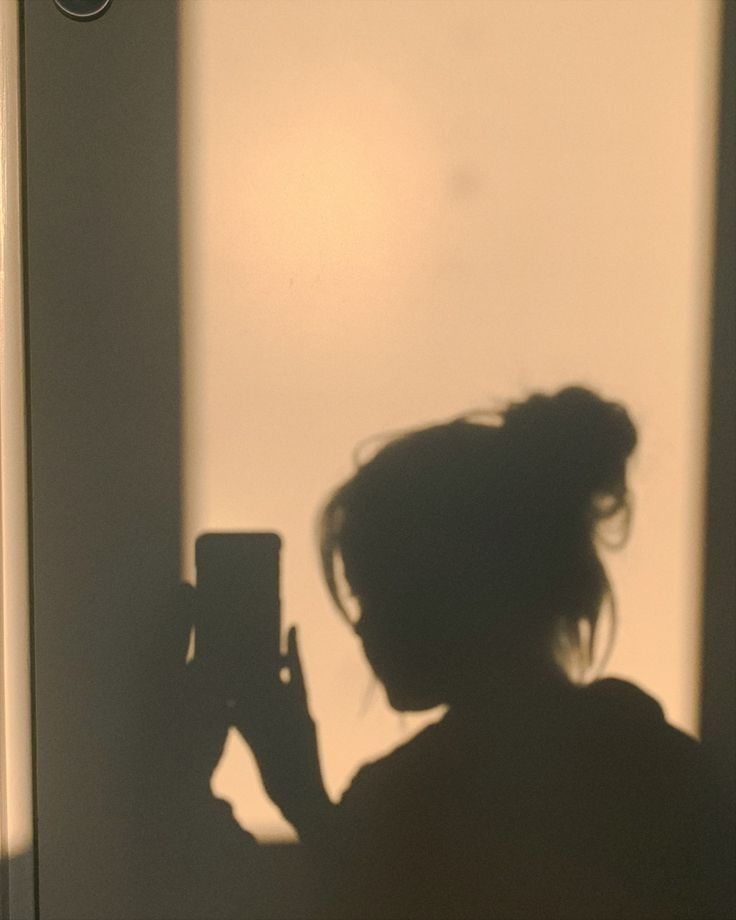 a woman taking a photo with her cell phone in the shadow from an open window