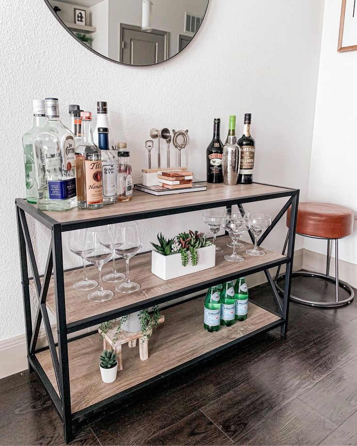 a bar cart with wine glasses and bottles on it in front of a round mirror