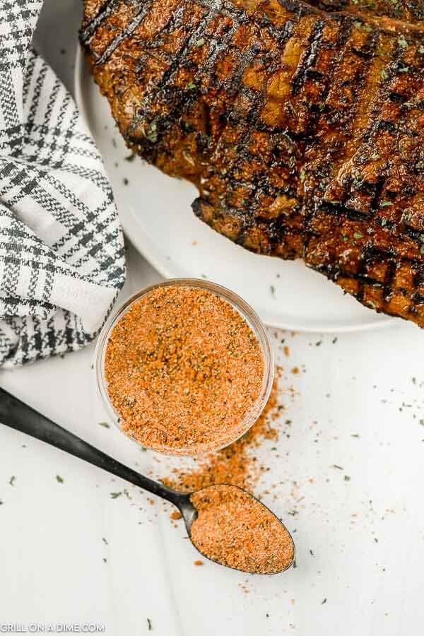 grilled steak on a plate with seasoning next to it and a spoon full of spices