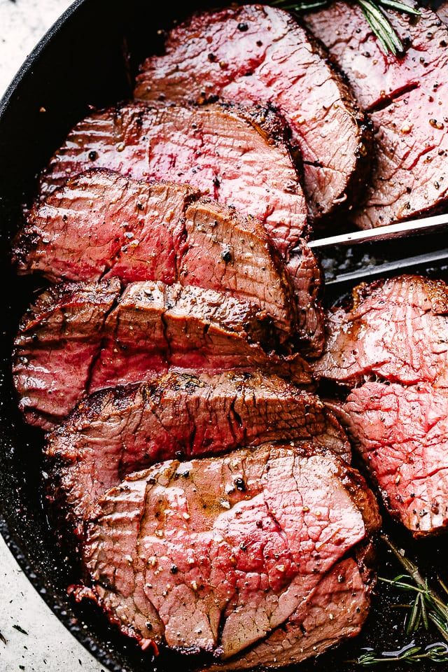 steaks in a skillet with tongs on the side and rosemary sprigs