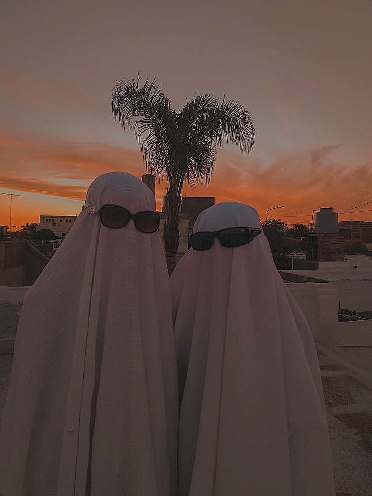 two people wearing sunglasses are standing in front of a palm tree with the sun setting behind them