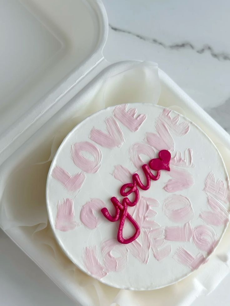 a white cake with pink icing and the word love spelled on it