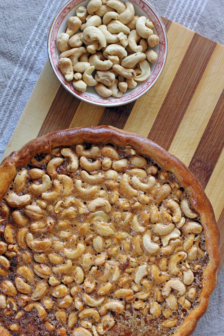 a pie sitting on top of a wooden cutting board next to a bowl of nuts