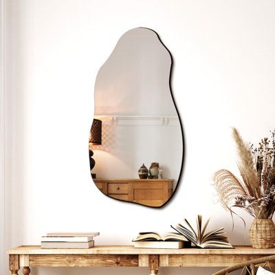 a mirror is hanging on the wall above a wooden table with books and vases