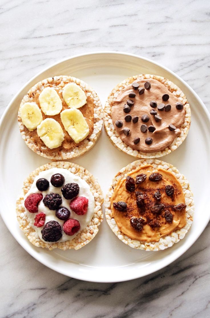 four desserts on a white plate with chocolate chips, bananas and other toppings