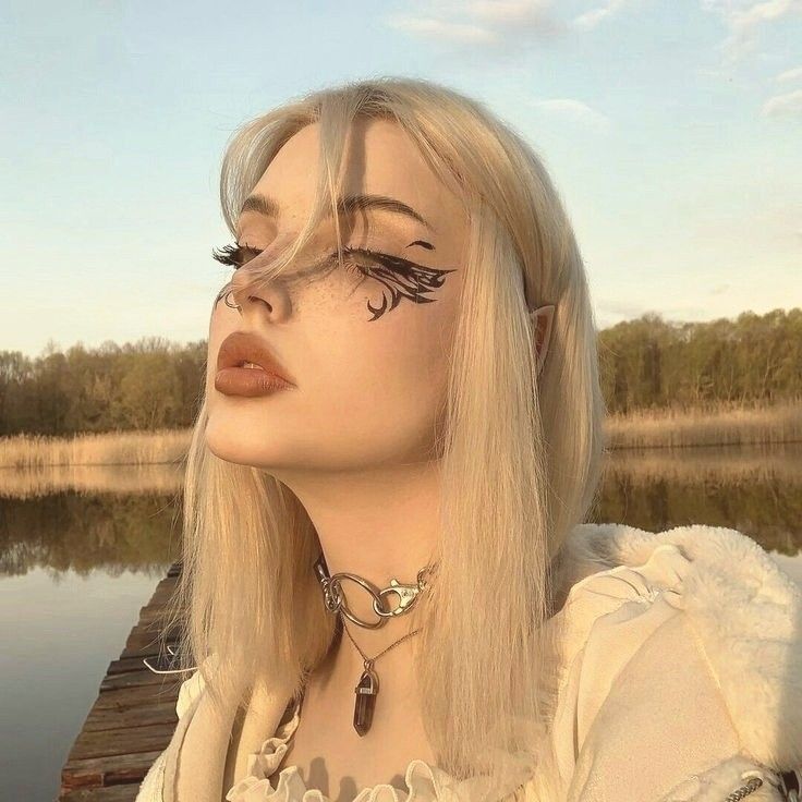 a woman with long blonde hair and black eyeliners is standing on a dock