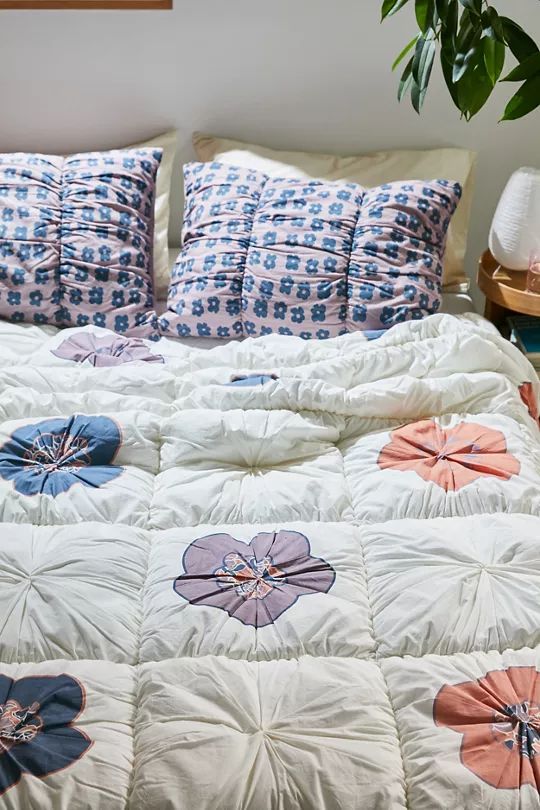 a bed with blue and pink flowers on the comforter next to a potted plant