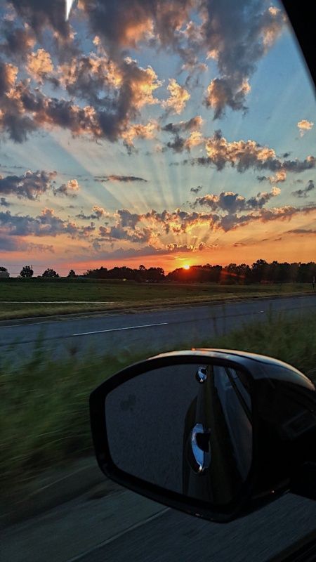 the sun is setting in the distance as seen from a car's side view mirror