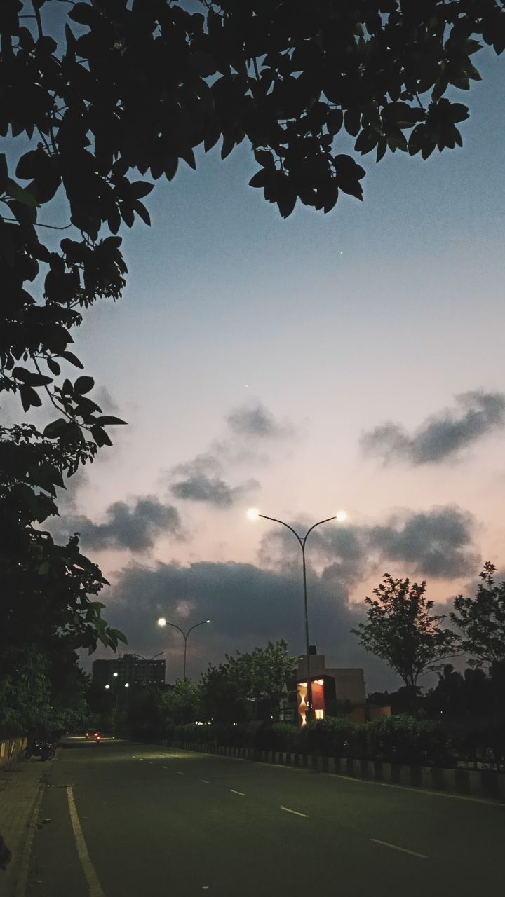 an empty street at night with the lights on and clouds in the sky behind it