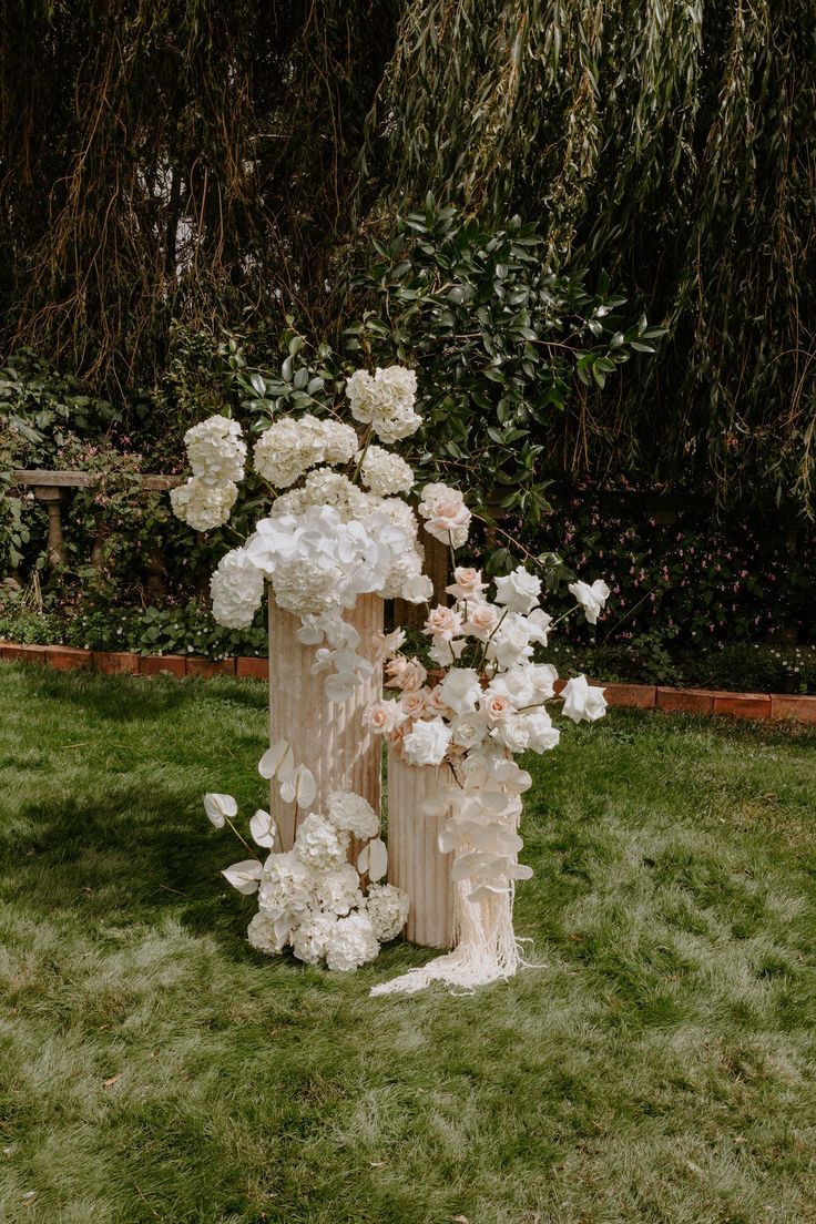 an arrangement of white flowers in a vase on the grass near some trees and bushes