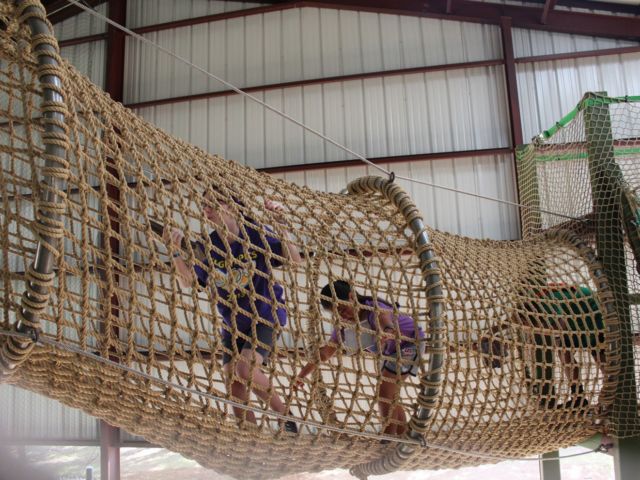 two people climbing on a rope course in an indoor play area with ropes and netting