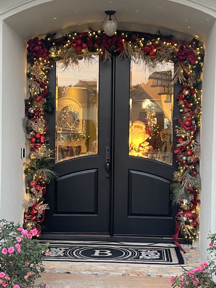 two black double doors with christmas decorations on them and wreaths hanging from the sides