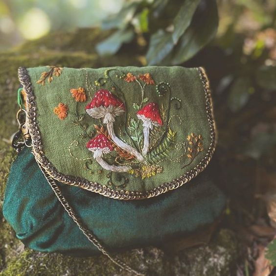 a green purse sitting on top of a mossy tree trunk with mushrooms embroidered on it