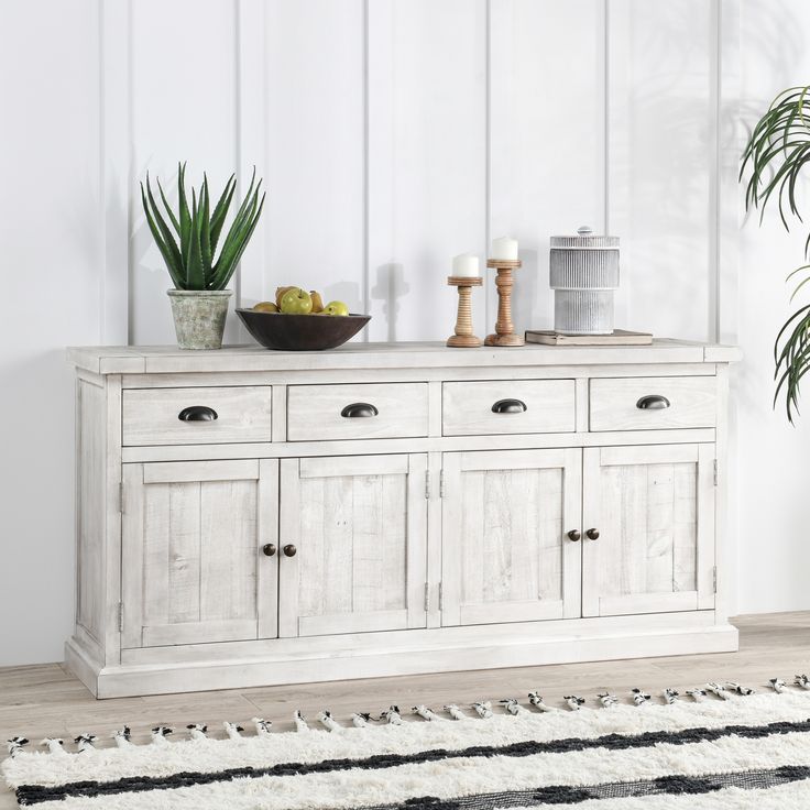 a white cabinet with two bowls on top and some plants in the corner next to it