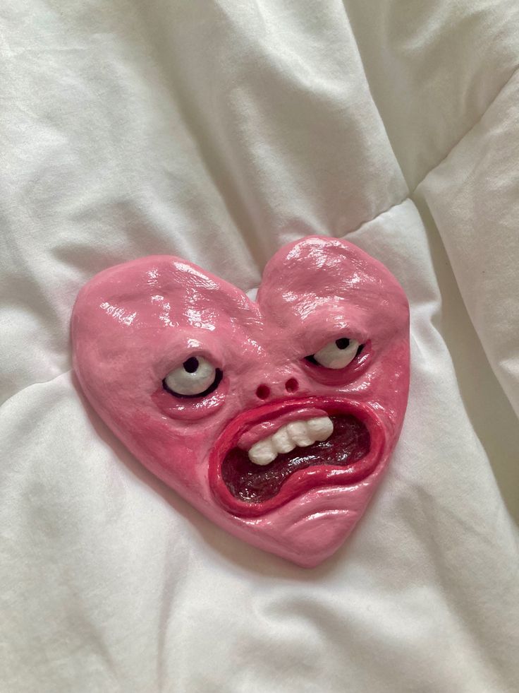 a pink heart - shaped object with eyes and mouth on a white sheet, lying on a bed