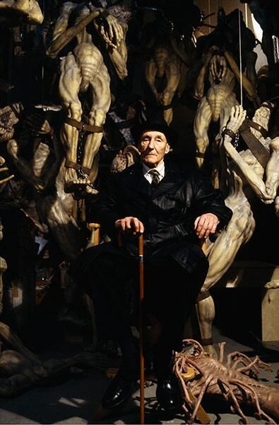 a man sitting on a chair in front of some creepy looking statues and other sculptures