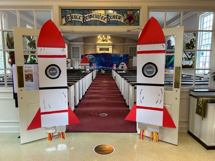 two cardboard rockets sitting on top of each other in the middle of a room filled with pews