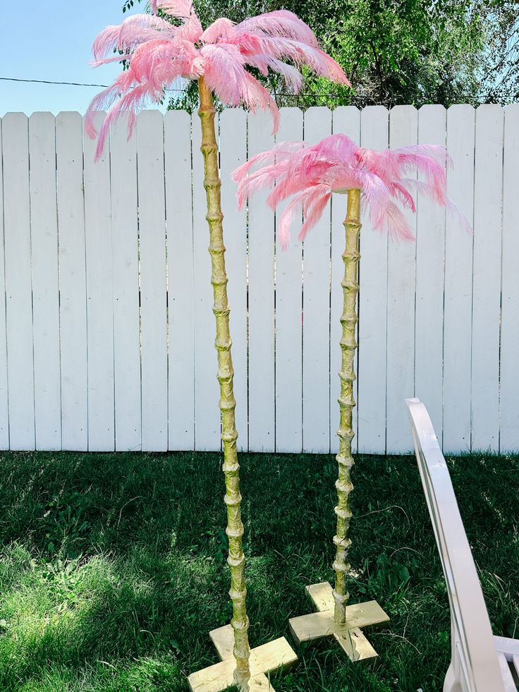 two tall pink palm trees in front of a white fence