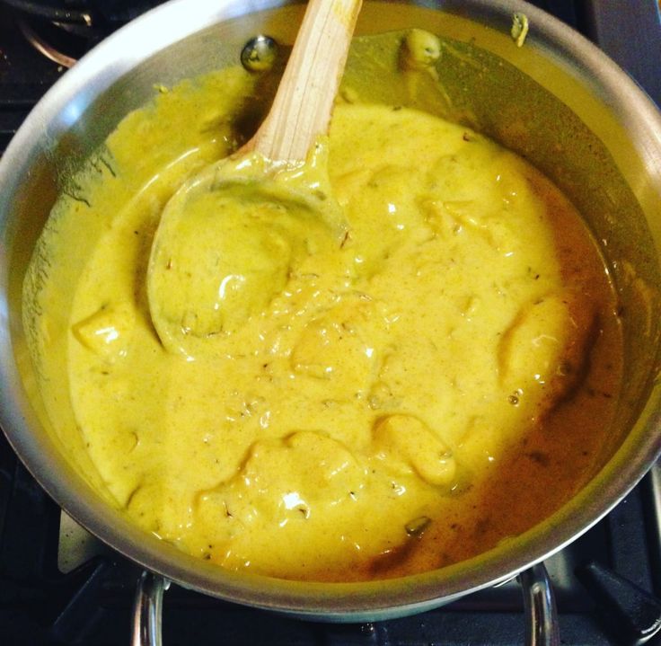 a pan filled with yellow sauce sitting on top of a stove next to a wooden spoon