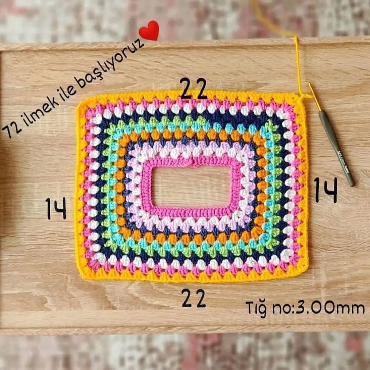 a crocheted square is shown on a wooden surface with scissors and thread next to it