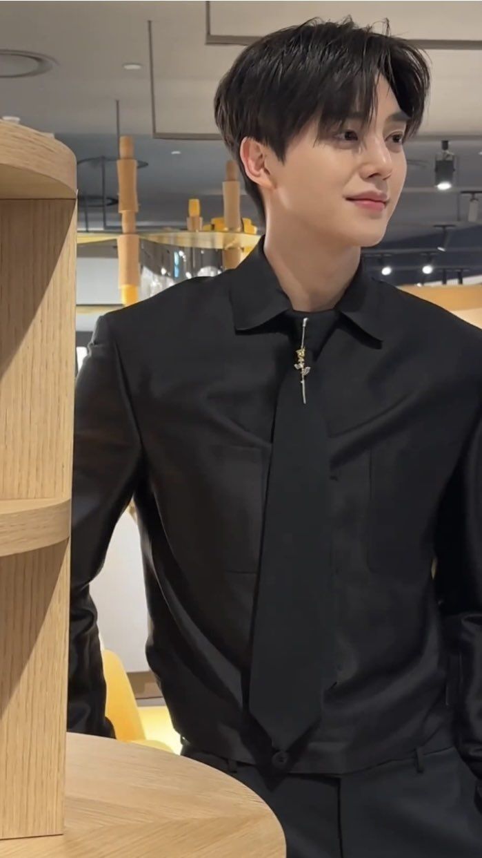 a young man wearing a black shirt and tie standing in front of a wooden shelf