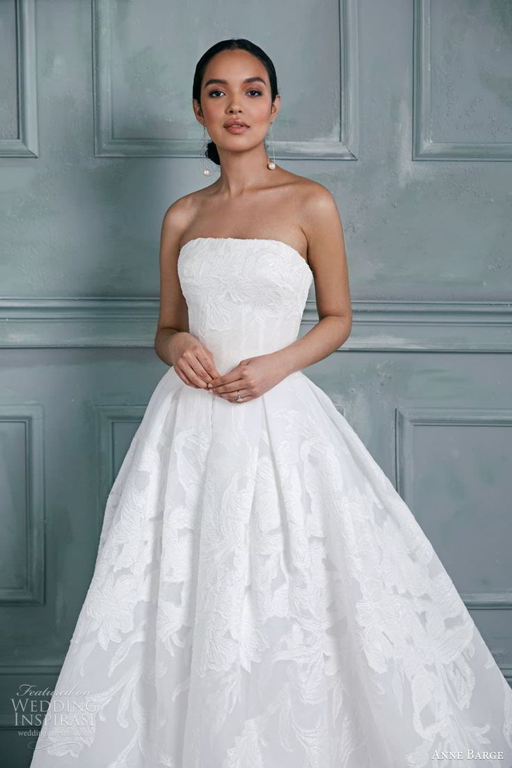 a woman in a white wedding dress standing next to a blue wall and wearing earrings