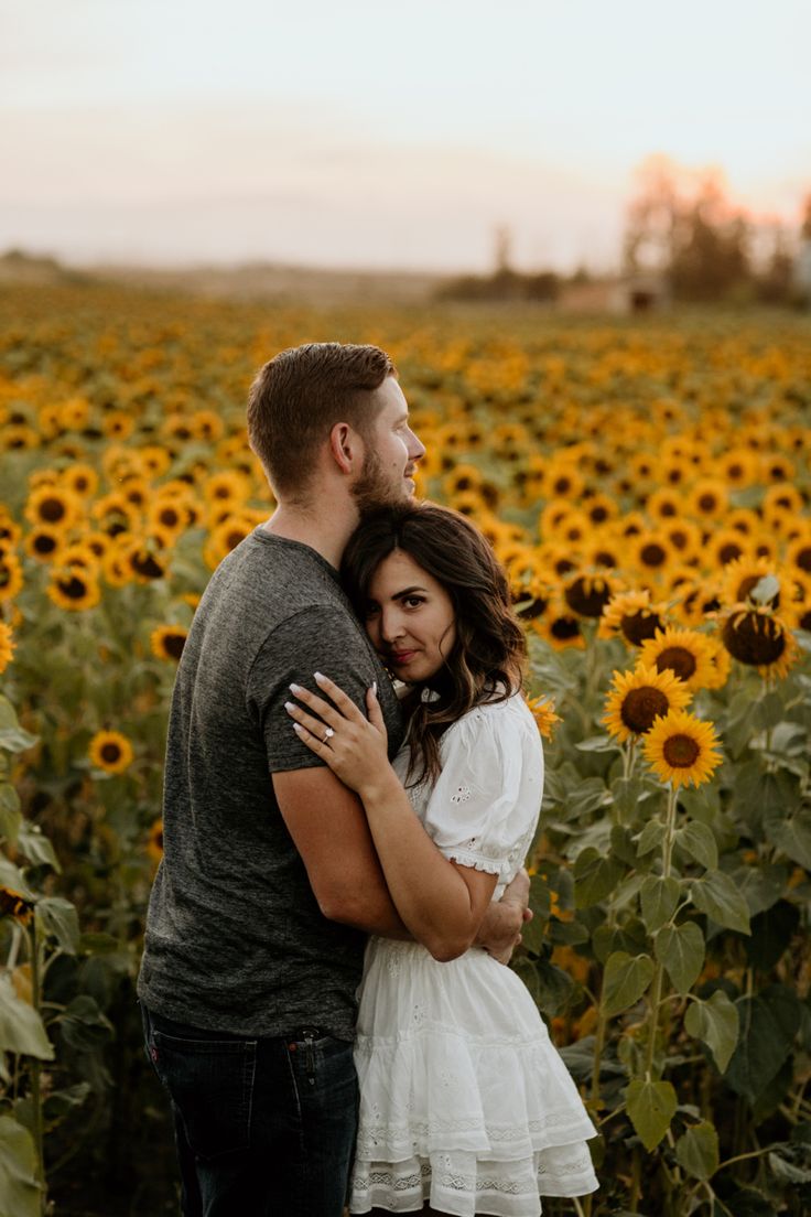 a man and woman standing in front of a field of sunflowers at sunset