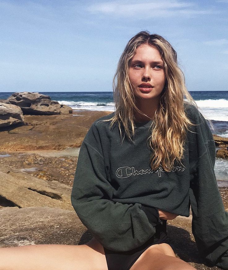 a woman is sitting on the rocks by the ocean with her legs crossed and looking at the camera