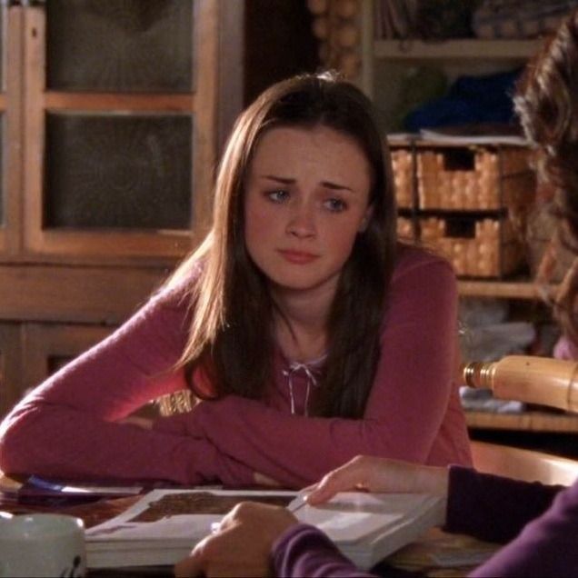 a woman sitting at a table in front of another woman who is holding a book